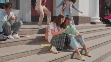 Okulun merdivenlerinde oturup tabletten bir şeyler izleyen çocukların el kameraları.