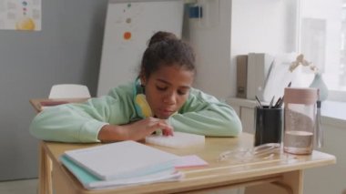 Sınıfta oturmuş duyusal oyuncaklarla oynayan, kulaklıklı 11 yaşındaki Afro-Amerikan bir kızın el kamerası görüntüsü.
