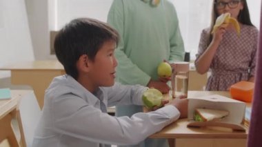 Asyalı öğrencinin el kamerasında, öğle tatilinde arkadaşlarıyla yemek yerken masada oturup elma yerken çekilmiş.
