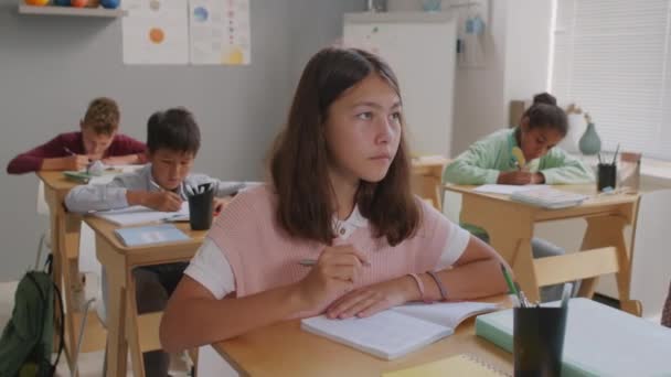 中学校の教室の机に座ってノートに書いている女の子と男の子の手による追跡 — ストック動画