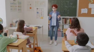 Yüz maskesi takan, öğretmenlik dersi veren ve soru soran bir kadınla el kamerası görüntüsü. Bir grup ortaokul öğrencisi de yüz maskesi takmış ellerini kaldırıyor.