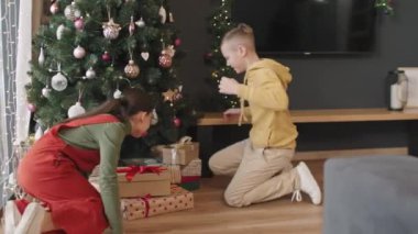 Güzel dekore edilmiş Noel ağacının altında oturmuş, hediye kutularını açmaya başlayan neşeli kardeşlerin mutlu ve şaşırmış fotoğrafları.