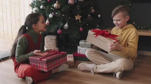 Vidám Testvérek Ülnek Gyönyörűen Díszített Karácsonyfa Alatt Kicsomagolják Dobozokat Ajándékokat — Stock videók