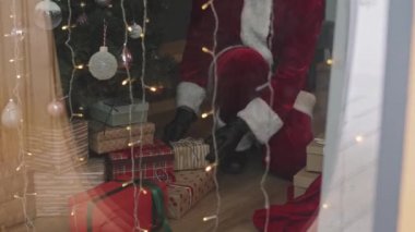 Noel Baba 'nın bir sürü Noel hediyesini evdeki güzel Noel ağacının altında kutulara koyarkenki görüntüsü.