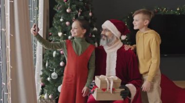 İki mutlu kardeşin Noel Baba 'yla akıllı telefonda kendi resimlerini çekerken orta yavaş çekimleri.