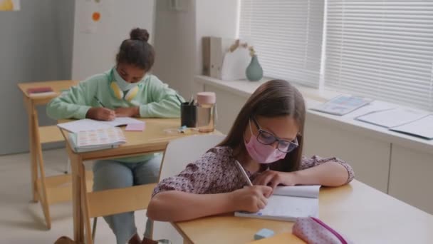 Orta Okuldaki Derste Maskeli Kızların Sıralarda Oturup Defterlerine Yazı Yazmalarını — Stok video