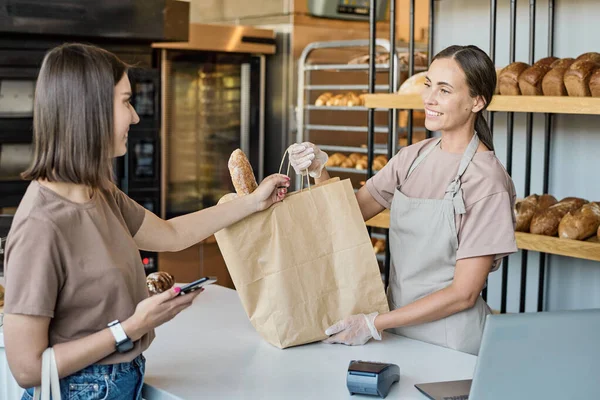 Sonriente joven hembra dando bolsa de panes — Foto de Stock