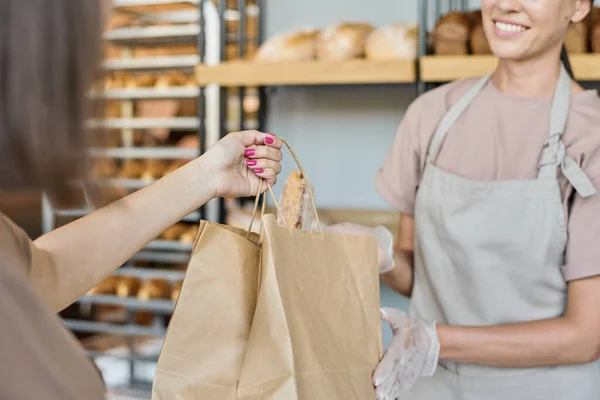 Jovem padeiro enluvado dando pão fresco assado — Fotografia de Stock