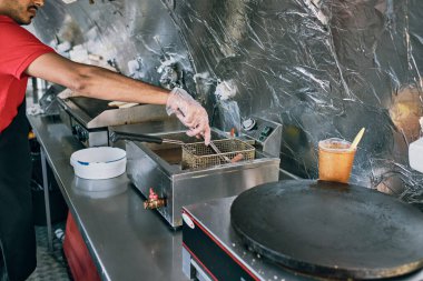 Eldivenli genç adam sosisi kızartma ekipmanına koyuyor.