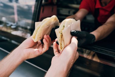 Lezzetli fast food yiyen genç adamın elleri kağıda sarılı.