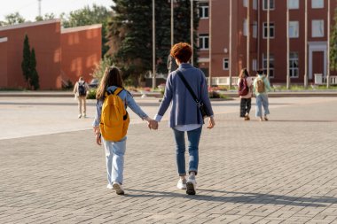 Sırt çantalı genç bayan ve kızı büyük meydanda ilerliyorlar.