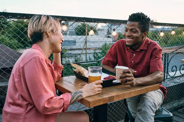 Feliz joven pareja intercultural tomando bebidas y aperitivos en la cafetería al aire libre —  Fotos de Stock