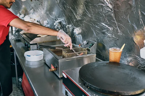 Молодой человек в перчатках кладет колбасу в оборудование для жарки — стоковое фото