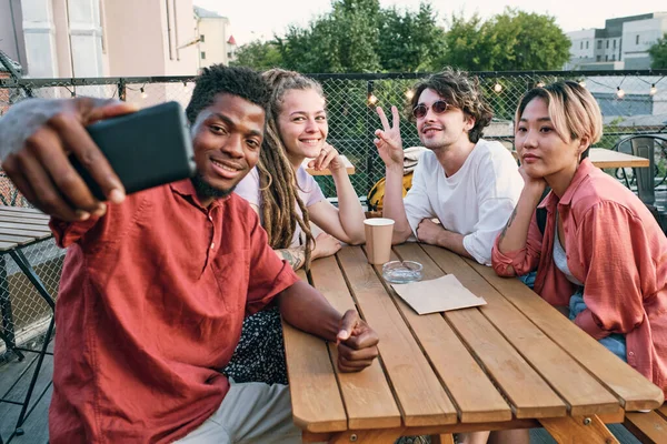 Happy African guy making selfie with intercultura friends by wooden table — Stock Photo, Image