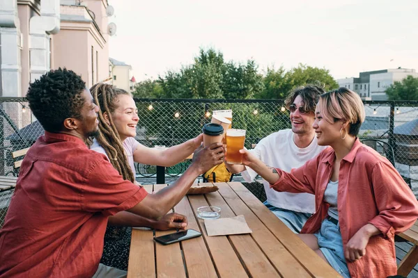 Jóvenes amigos interculturales brindando con bebidas sobre mesa de madera —  Fotos de Stock