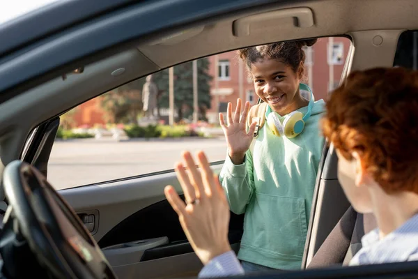 Lächelndes Schulmädchen winkt ihrer Mutter beim Aussteigen aus dem Auto zu — Stockfoto