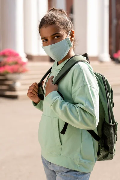 Милая афроамериканская школьница в рюкзаке в защитной маске — стоковое фото
