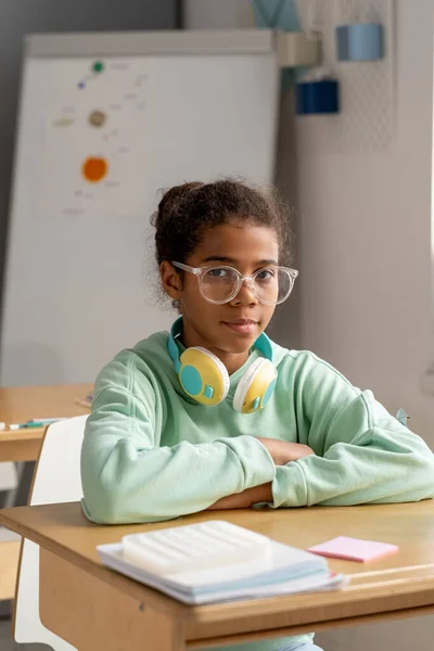 Χαριτωμένη σοβαρή μαθήτρια με γυαλιά που κάθεται στο γραφείο της. — Φωτογραφία Αρχείου