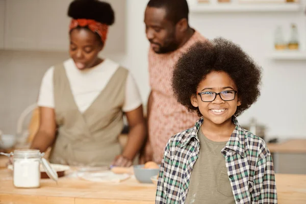 Glad pojke i glasögon ler mot sina föräldrar matlagning — Stockfoto