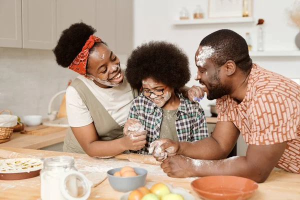 Divertida familia joven de tres con harina en la cara jugando mientras cocinan pastelería casera —  Fotos de Stock