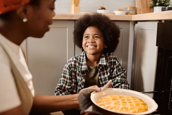 Menino alegre olhando para sua mãe tomando torta de maçã fresca quente fora do forno elétrico — Fotografia de Stock