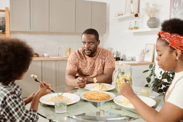 Jovem família sentada à mesa servida e jantar na cozinha — Fotografia de Stock