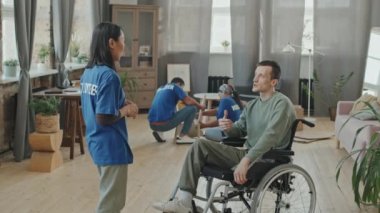 Engelli bir adamın gönüllü gruptan genç Asyalı bir kadınla el sıkışırken orta yavaş çektiği fotoğraf. Dairedeki mobilyaların montajına ya da onarımına yardım etmeye geldi.