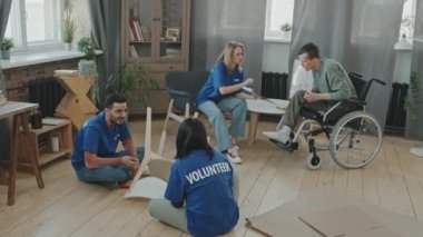 Mavi tişörtlü gönüllülerden oluşan yüksek açılı yavaş çekim. Evinde tekerlekli sandalyede oturan engelli bir genç için mobilya topluyorlar.