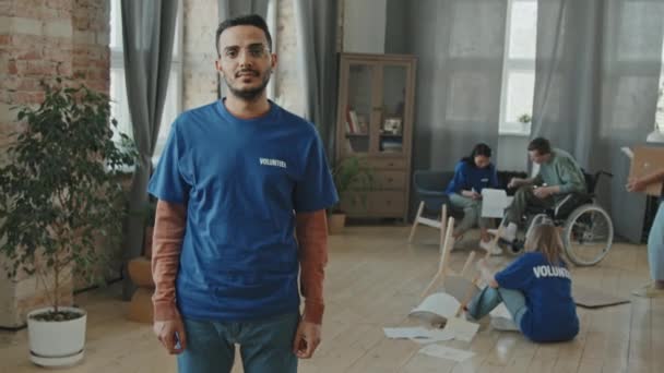 身着蓝色T恤 双臂交叉摆姿势的中东年轻男性志愿者的缩影 与他的团队一起帮助家中残疾男子走来走去 — 图库视频影像