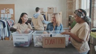 Gönüllü organizasyondan üç kadının, plastik konteynırlardan yapılan bağışları sıralarken, erkeklerin ağır karton kutular taşıdığı orta boy, yavaş çekim.
