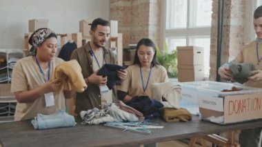 Genç, çok ırklı erkek ve kadın gönüllülerden oluşan bir grubun plastik konteynırlardaki bağışlanan eşyalara bakıp, hayır kurumlarına bağışlamadan önce onları sıralaması.