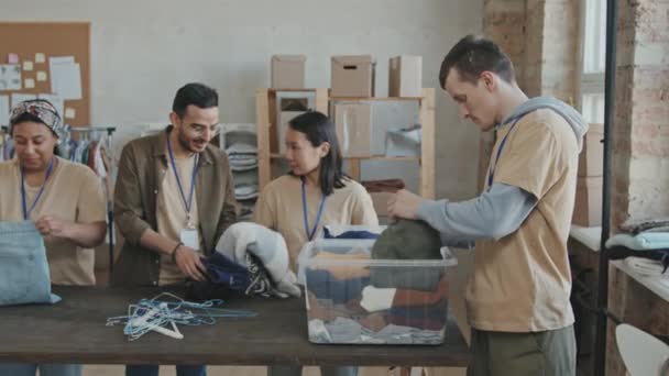 Mediana Slow Shot Joven Voluntario Masculino Clasificando Ropa Donada Con — Vídeos de Stock