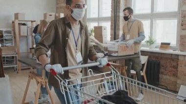 Yüzü maskeli gönüllülerden oluşan yavaş çekim. Yardım için bağışlanan kıyafetleri düzenliyorlar. Modern çatı katı tarzı stüdyoda birlikte çalışıyorlar.