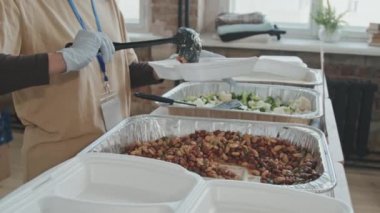 Tanınmayan gönüllülerin orta bölüm yavaşlaması evsizlere ve muhtaçlara yiyecek sağlamak için plastik konteynıra koymaları.