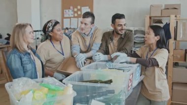 Geri dönüşüm konteynerlerindeki çöpleri sıralarken kameraya gülümseyen erkek ve kadın gönüllülerden oluşan genç çoklu etnik grubun yavaş portresi