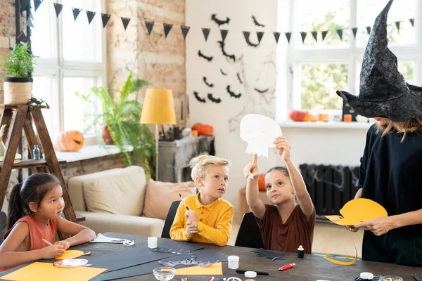 Kleines Mädchen zeigt auf das Halloween-Symbol aus Papier, während es es es dem niedlichen Jungen zeigt — Stockfoto