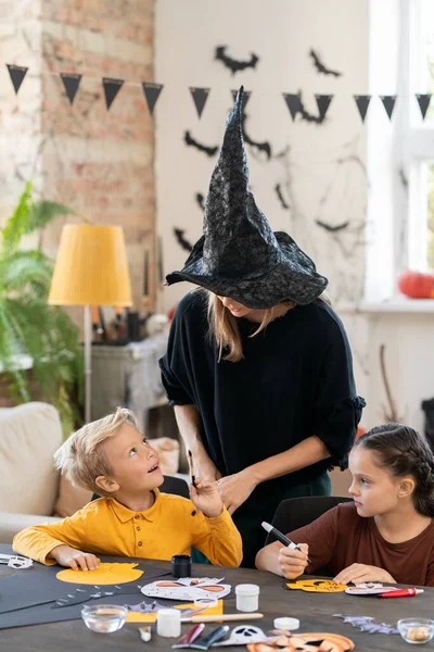 Netter Junge mit Pinsel schaut Lehrerin mit Hexenhut an — Stockfoto