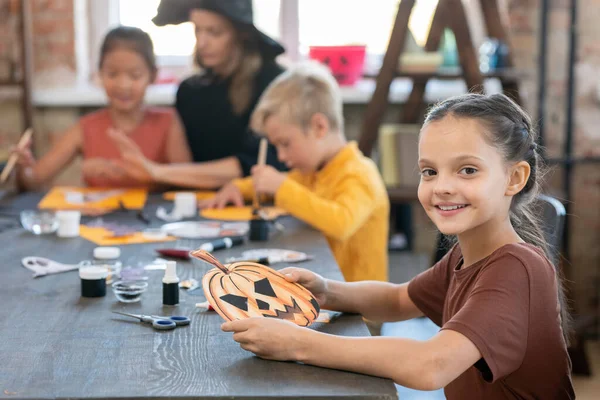 Glückliches kleines Mädchen mit dem Symbol von Halloween am Tisch sitzend — Stockfoto