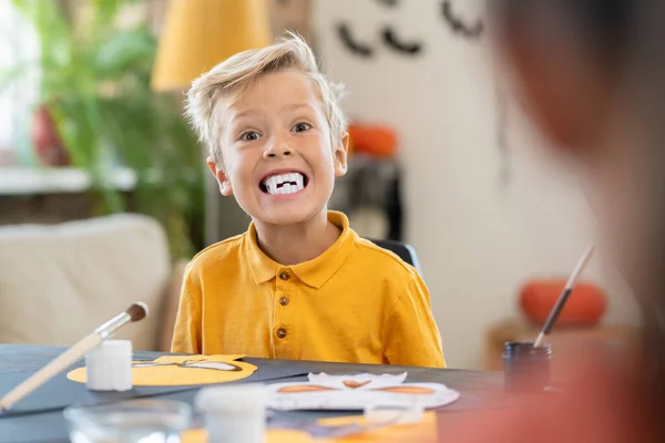 Gruseliger Junge mit weißen Reißzähnen blickt an einem Tisch in die Kamera — Stockfoto