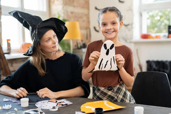 Liebenswertes Mädchen zeigt Papiergespenst und schaut in die Kamera — Stockfoto