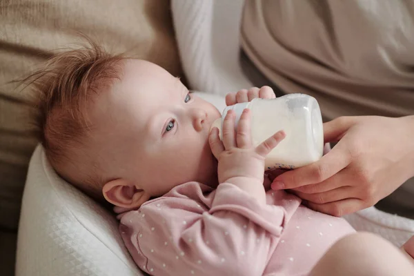 Милая малышка ест молоко, держа бутылочку. — стоковое фото