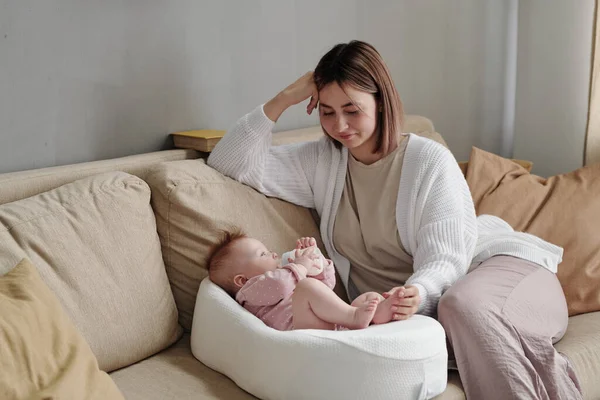 Joyeux jeune mère assise sur le canapé à côté de sa fille bébé — Photo