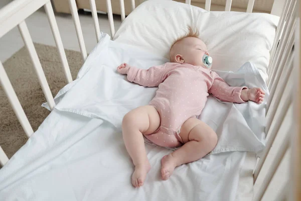 Spokojne niemowlę w różowych ubraniach leżące na białej pościeli w łóżeczku — Zdjęcie stockowe