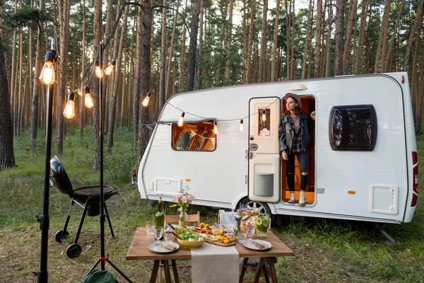 Jeune femme dans la maison sur roues parmi les pinetrees et servi table en face — Photo