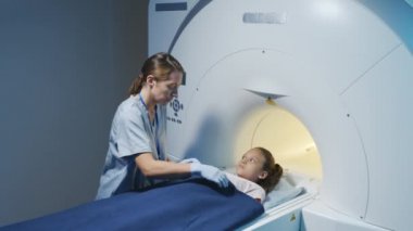 Modern kliniğin radyoloji odasında küçük bir kızı muayene ederken kadın MRI teknisyeninin yavaş çekimleri.