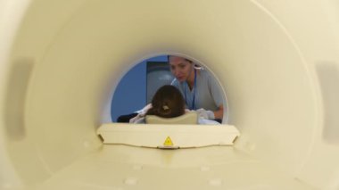 Kadın radyolojistin muayene yapmadan önce MRI tarayıcı tüpünün içinde hastayla konuştuğu yavaş çekim.