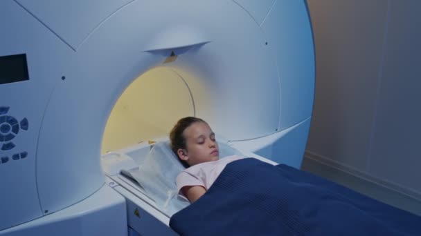 扫描台上的小女孩慢镜头进入Mri机 在有蓝光的现代放射科病房进行检查 — 图库视频影像