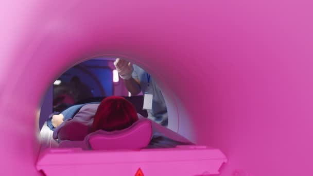 検査のため紫のライティングでMriチューブに寝そべっている若い女性のスローショット 患者の世話をする男性医師 — ストック動画