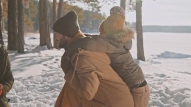 Küçük kızını sırtında taşıyan ve kış günü ormanda dönen mutlu bir adamın el bilgisayarı.