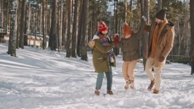 Güneşli kış gününde karda yürürken küçük kızı kollarıyla kaldıran mutlu adam ve kadının yavaş çekimleri.